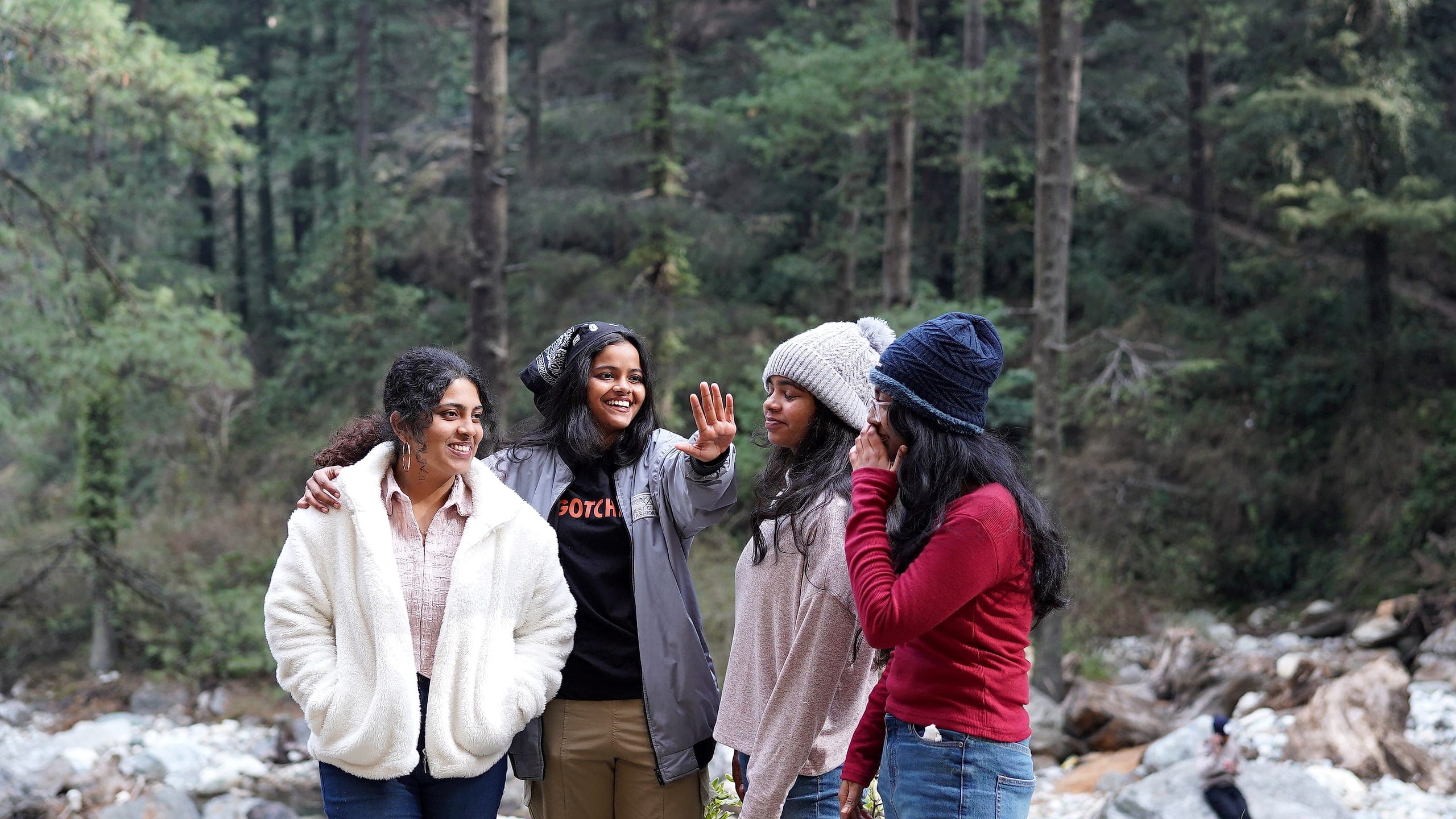 Four travellers laughing together in a deodar forest beside a river in Himachal Pradesh